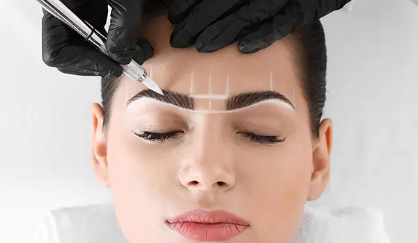 Trainee applying microblading strokes with precision tool on mapped eyebrow, learning professional technique
