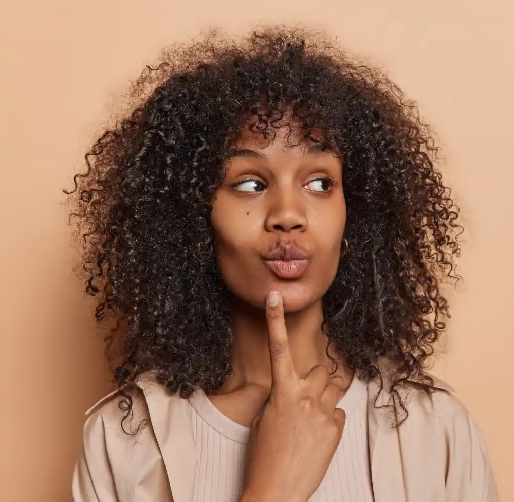 A woman with a thoughtful expression, representing a client preparing a list of questions to ask during a lip tattoo consultation.