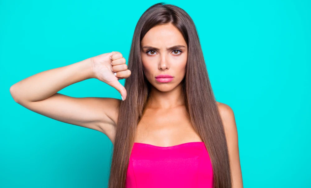 An unhappy woman gives a thumbs-down, representing the negative experiences and regrets some clients have with lip blushing.