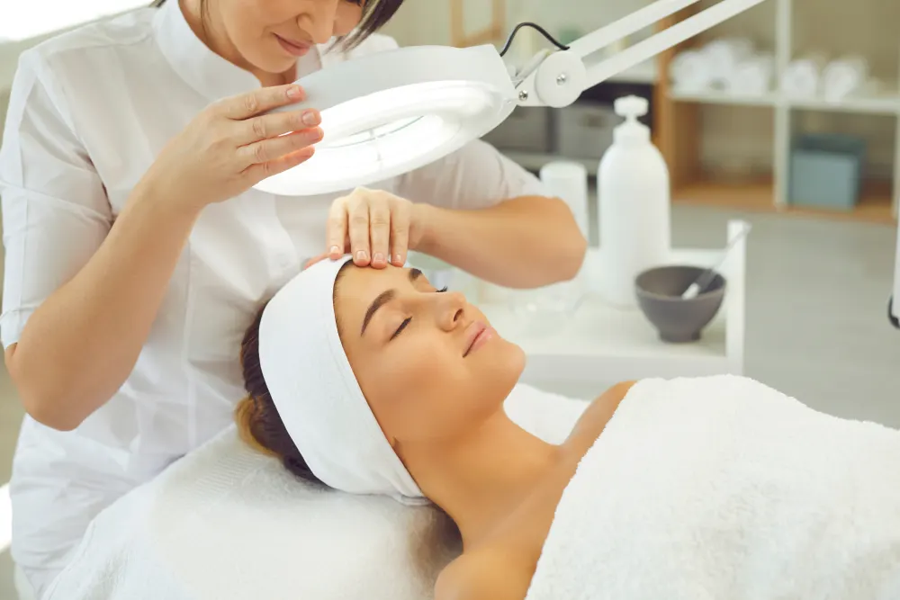 A lash technician uses a magnifying lamp to closely assess the condition of a client's natural lashes before a procedure.