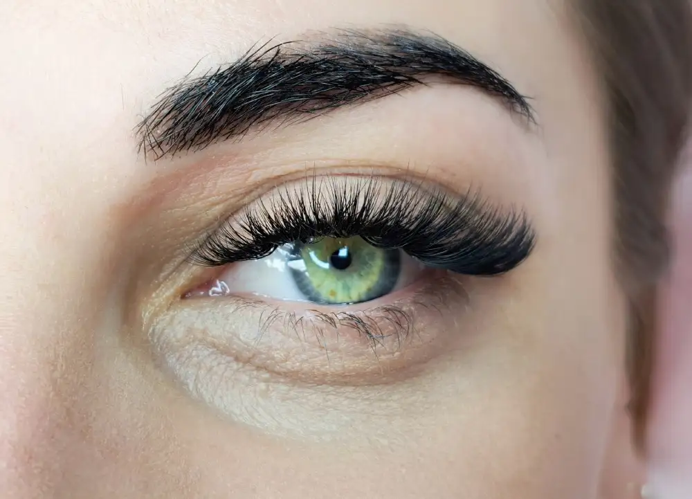 A close-up of a green eye with dense volume eyelash extensions, creating a bold and striking look favored by many clients.